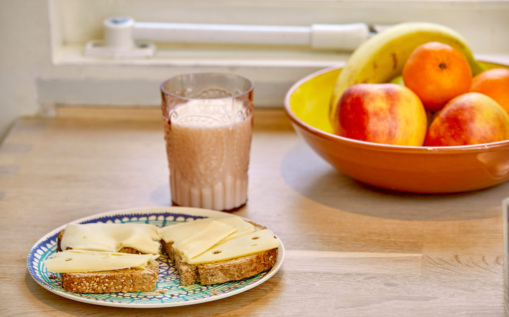 Boterham met kaas, een glas melk en een fruitschaal.